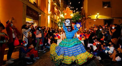 Personas caracterizadas con maquillaje, flores y vestidos celebrando el origen del Día de Muertos