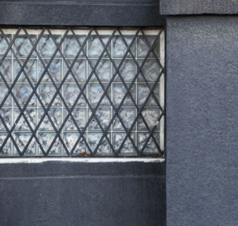 Protecciones de herrería con un patrón de rombos pintados de negro sobre una ventana de bloques de vidrio