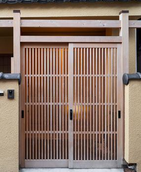 Puerta de herrería elaborada con perfiles delgados de color café en el exterior de una casa