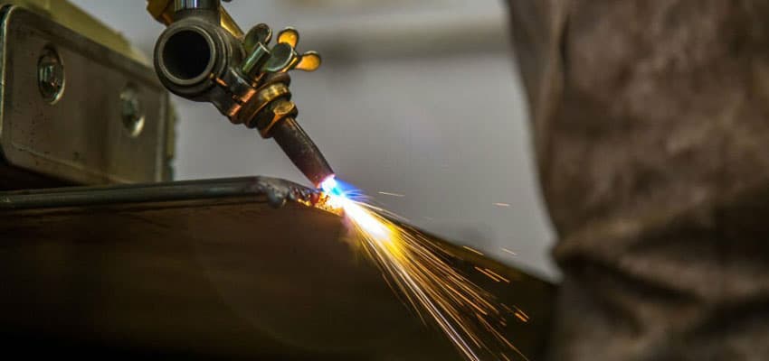 Acercamiento a un trabajador realizando la técnica de oxicorte sobre una placa de acero