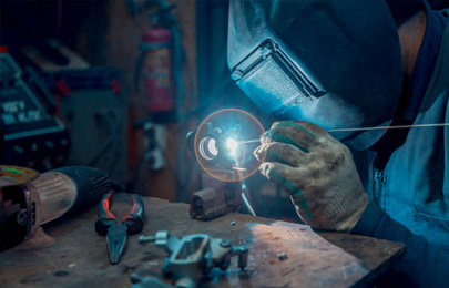 Herrero con equipo de protección en su taller realizando soldadura TIG en una pieza de aluminio